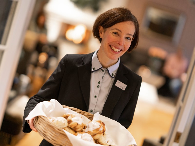Smilende dame med navnskilt holder et stort fat med kanelsnurrer