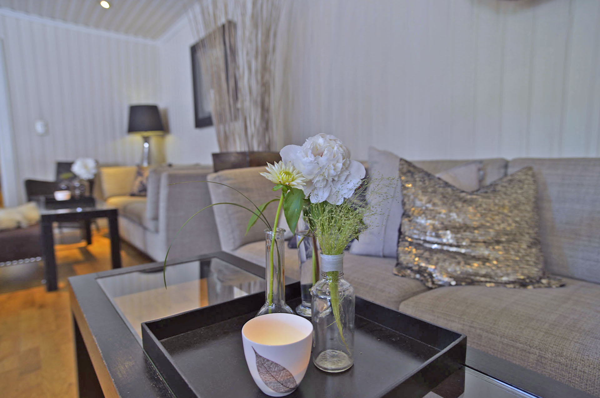 To grå sofaer ved siden av hverandre med tente telys på bordene