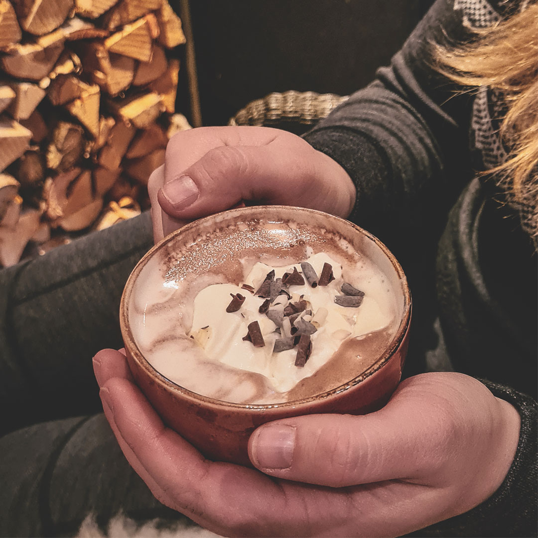 Nærbilde av kopp med kakao holdt av to hender