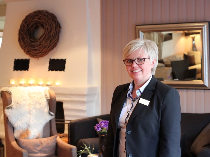 Kvinne i sort dressjakke står i en stue