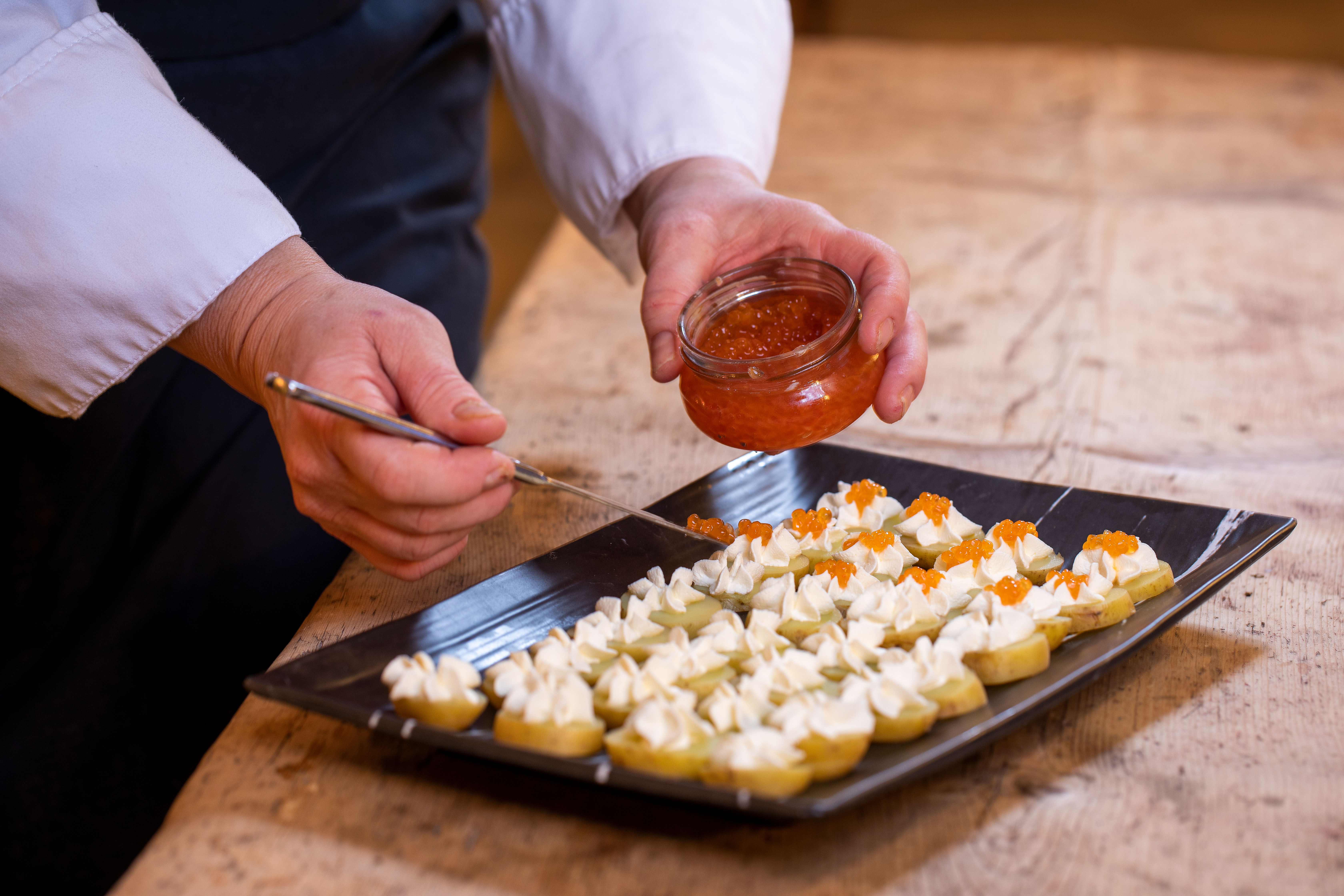 Et par hender bruker en skje til å fordele ut ørretrogn på potetskiver med rømme